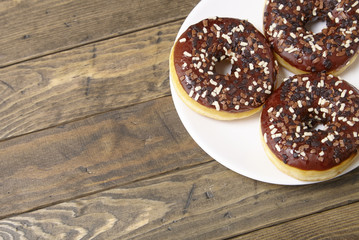 A plate of iced chocolate sprinkle ring donuts on a rustic wooden table background with blank space at side