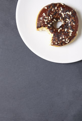 An iced chocolate sprinkle ring donut with bite mark, on a rustic slate background with empty space below