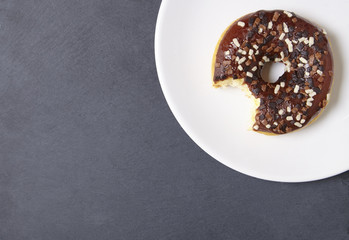 An iced chocolate sprinkle ring donut with bite mark, on a rustic slate background with empty space at side