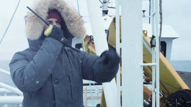 Adventurer in Warm Jacket Standing on Ship and Using Radio for Communication. It is Snowy and Windy.  Shot on RED Cinema Camera in 4K (UHD). 