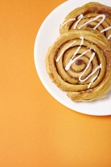 A plate of freshly baked cinnamon swirls on a bright orange background with blank space below