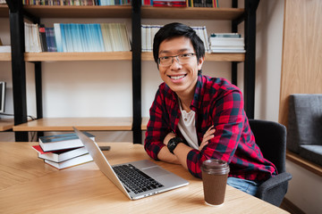 Asian man using laptop at the library and drinking coffee