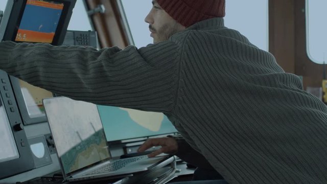 Captain of Commercial Fishing Ship Surrounded by Monitors and Screens Working with Sea Maps in his Cabin. Shot on RED Cinema Camera in 4K (UHD). 