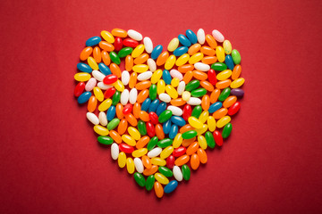 Big heart from colorful candies on red paper background. 