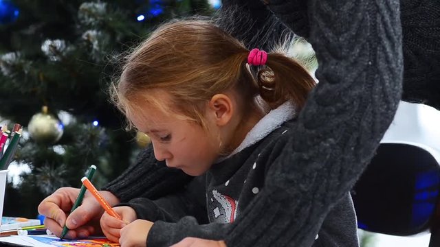 Father helping her daughter in drawing. Watching little girl drawing on paper. Christmas lights background