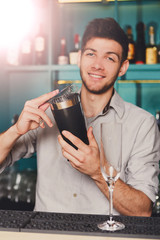 Young handsome barman in bar shaking and mixing alcohol cocktail