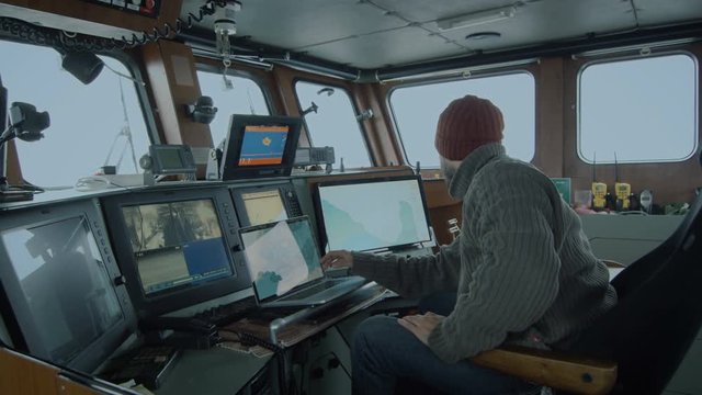 Captain of Commercial Fishing Ship Surrounded by Monitors and Screens Working with Sea Maps in his Cabin. Shot on RED Cinema Camera in 4K (UHD). 