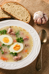Traditional polish white borscht - zurek, sour soup with white sausages and eggs.