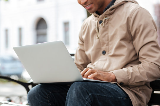 Young african man with laptop sitting on wooden bench