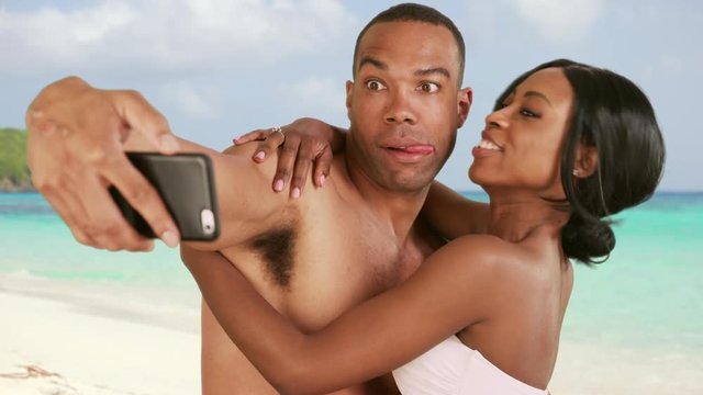 Engaged couple on honeymoon taking selfies on Caribbean beach