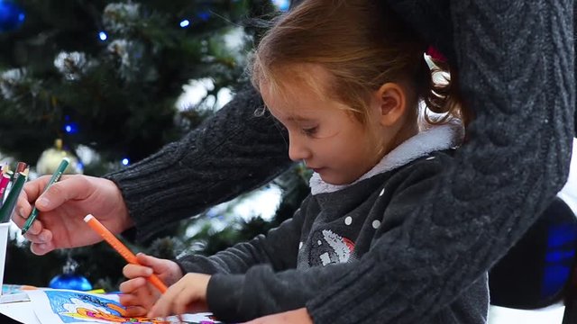 Father helping her daughter in drawing. Watching little girl drawing on paper. Christmas lights background