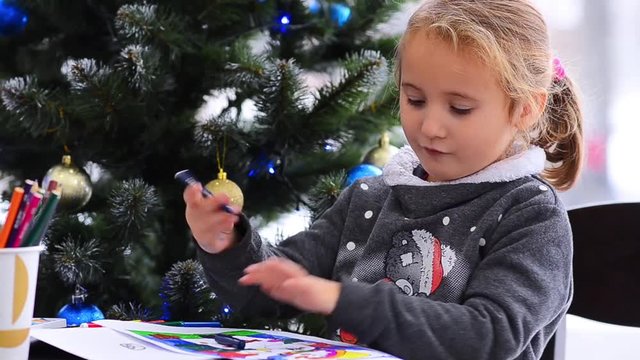 Cute happy little girl playing with crayons. Christmas background. Christmas lights background