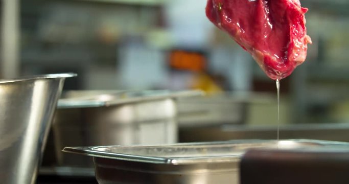 Cooking process on restaurant kitchen 4k video. Raw meat bone steak, chef hand with food tongs, steel professional tools cookware