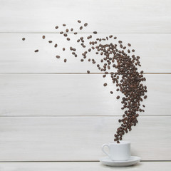 White cup and coffee beans scattered on wooden background