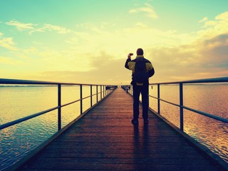 Man photograph morning sea from long wooden mole in wharf.