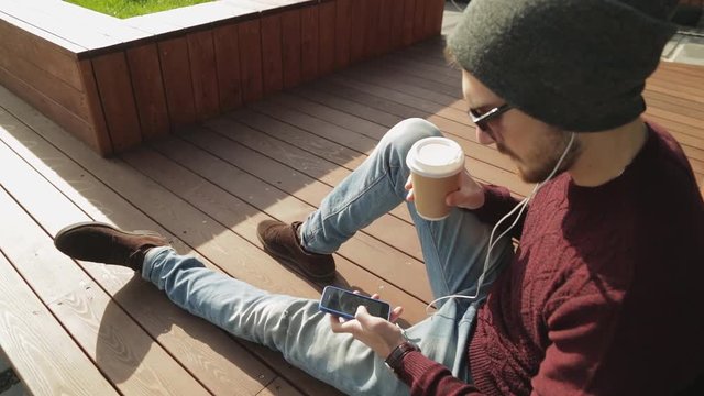 Handsome hipster using app and listening to music in smartphone headphones