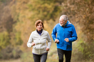 Beautiful senior couple running outside in sunny autumn forest