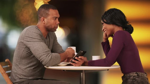African American couple drinking coffee and browsing internet on smartphones on date