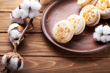 Creme brulee macaroons at a ceramic plate and cotton flowers on a wooden table. Soft light. Close view.