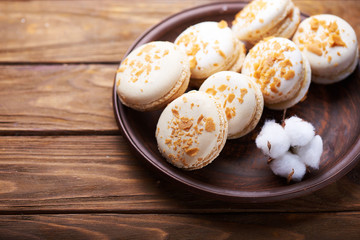 Creme brulee macaroons at a ceramic plate and cotton flowers on a wooden table. Soft light. Close view. Space for text