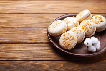 Creme brulee macaroons at a ceramic plate and cotton flowers on a wooden table. Soft light. Close view. Space for text