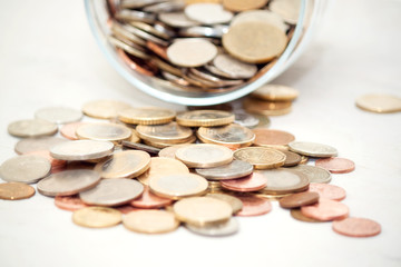 glass savings jar filled with coins on white table.