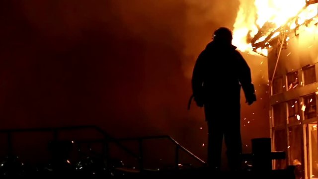 House building on fire at night. Inferno conflagration. Fireman fights fire.
