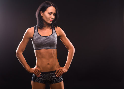Sports, fitness, athletics concepts. Picture of smiling brunette fitness lady showing her perfect abs and posing with her hands on hips.