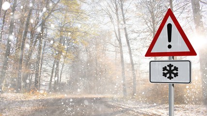 snow warning street sign on a snowy forest road with dark trees and sunbeams on  late winter day