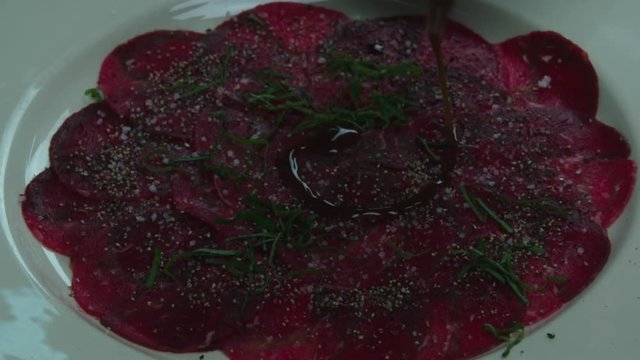 Serving carpaccio meat dish with sauce HD slow motion сlose up video. Sauce pouring on raw beef slices. Cooking on restaurant kitchen 