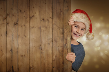 Lachender Junge mit Weihnachtsmütze hinter Holzwand