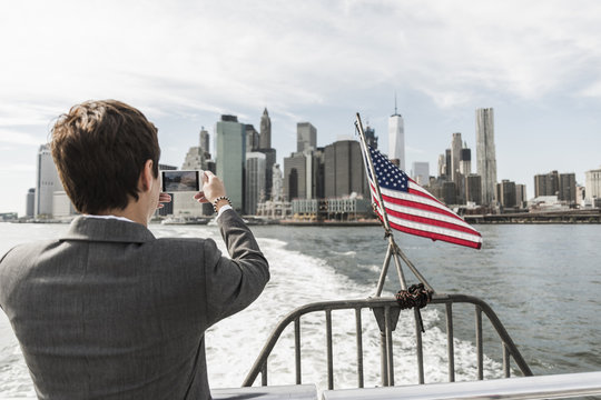 USA, Brooklyn, back view of businesswoman on a boat taking picture of Manhattan skyline