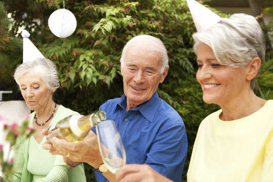 People celebrating in garden, senior man pouring champagne in glass