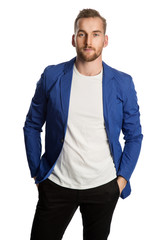 Trendy blonde man wearing a bright blue blazer and dark jeans, standing against a white background smiling towards camera.