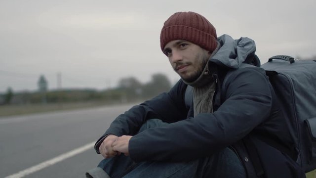 Casualy Dressed Traveler Sitting by the Highway at a Cloudy Day. Shot on RED Cinema Camera in 4K (UHD). 