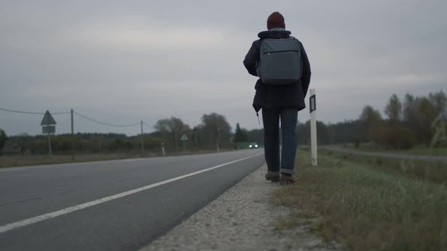 Casualy Dressed Traveler Sitting by the Highway at a Cloudy Day. Shot on RED Cinema Camera in 4K (UHD).