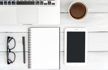 White office desk with laptop, smartphone, and notebook on wooden table. Top view with copy space. Student or business accessories flatlay. Office supplies and gadgets on background. View from above.
