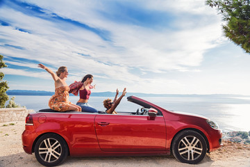 Group of happy young people waving from the red convertible.