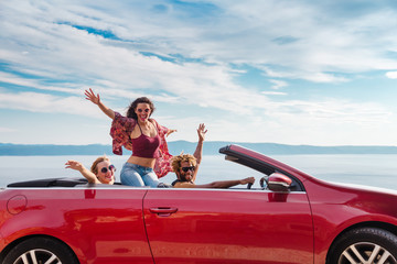 Group of happy young people waving from the red convertible.