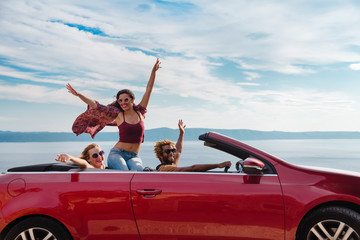 Group of happy young people waving from the red convertible.