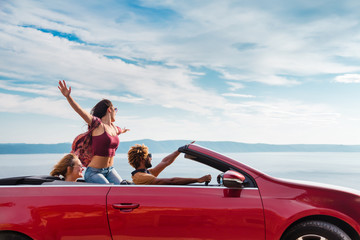 Group of happy young people waving from the red convertible. - 128747111