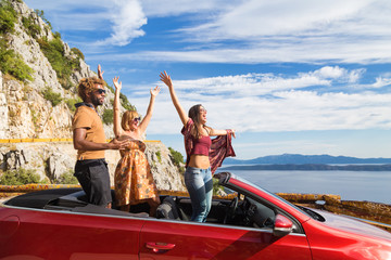 Fototapeta premium Group of happy young people waving from the red convertible.