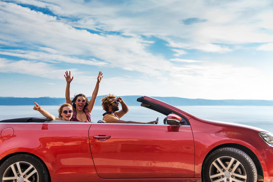 Group of happy young people waving from the red convertible.