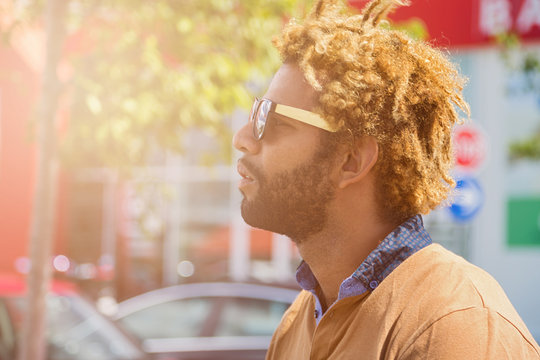 Portrait of young black man with dread locks wearing sunglasses. Sun effect applied.