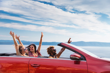 Group of happy young people waving from the red convertible.