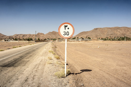 Iran, Gameh: Iranian traffic sign speed limit 30 kilometers in the desert with mountains  an oasis village in the background