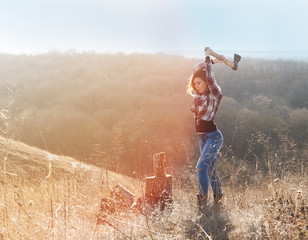 Beautiful sexy smiling woman in jeans and checkered shirt chopping wood with ax