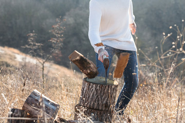 Man in jeans and sweater chopping wood with ax