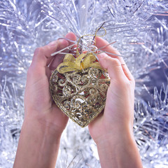 Female hands holding beautiful Christmas heart ornament in front of Christmas tree