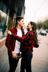 Two happy trendy teenage friends walking and dancing in the city, listening to the music with headphones, talking each other and smiling. Lifestyle, friendship and urban life concepts.